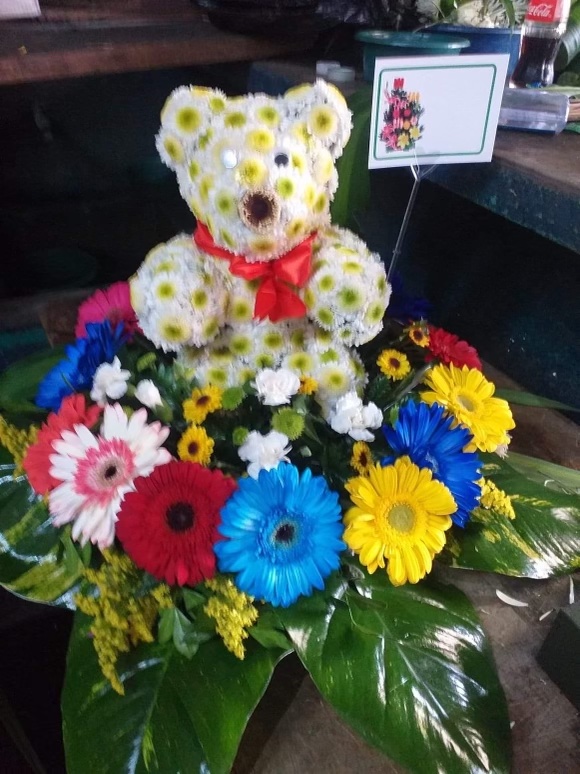 An image of red, white, and blue daisies along with, a teddy bear made out of white and yellow daisies