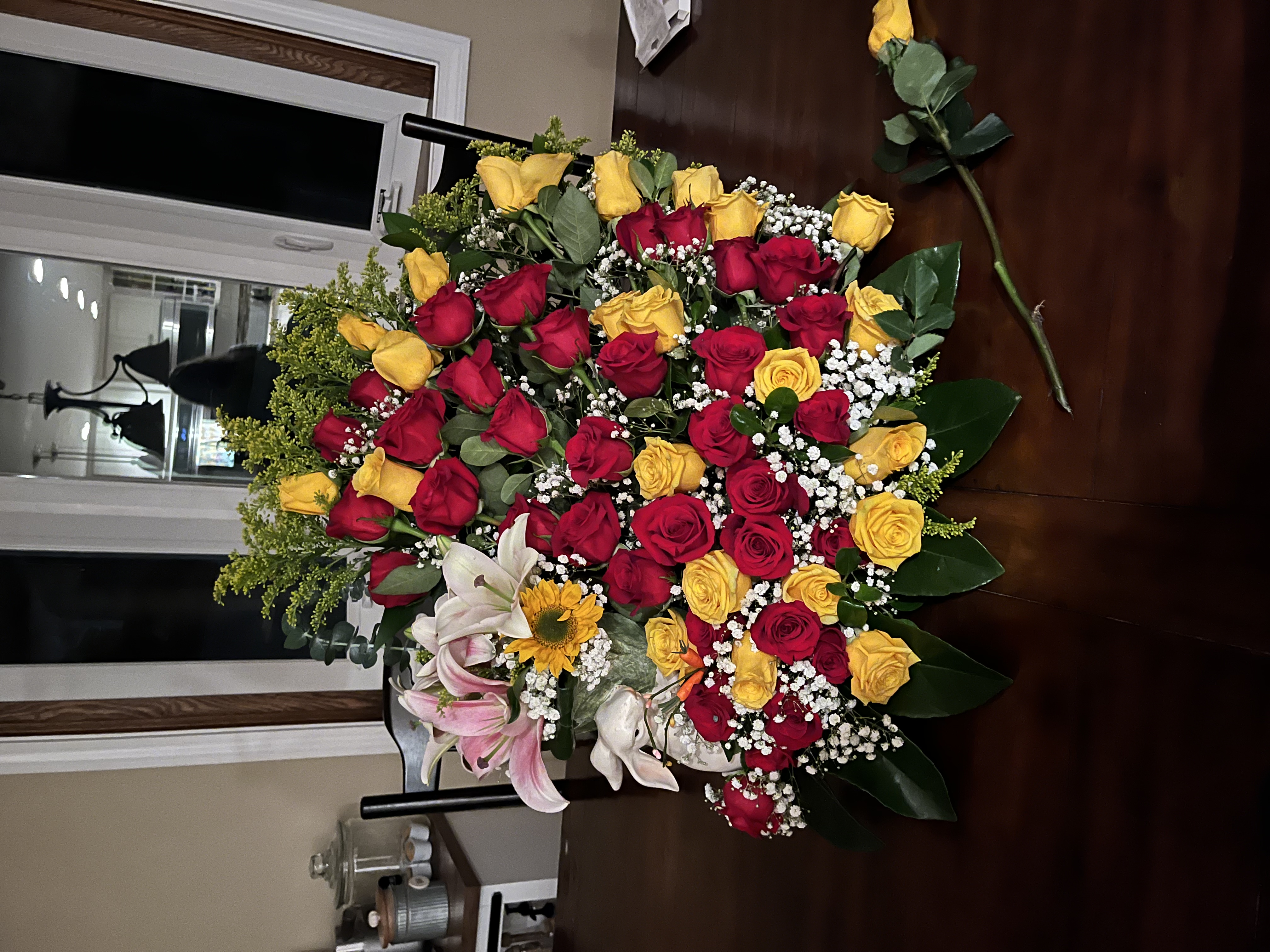 An image of yellow and red roses made into an arrangement with a lovely ceramic bunny by its side